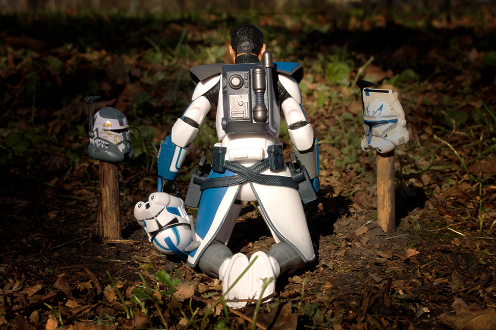  Photo of clone trooper from Star Wars kneeling at a gravesite marked by fellow troopers' helmets.